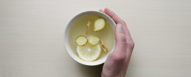 person holding white bowl with sliced lime and ginger inside